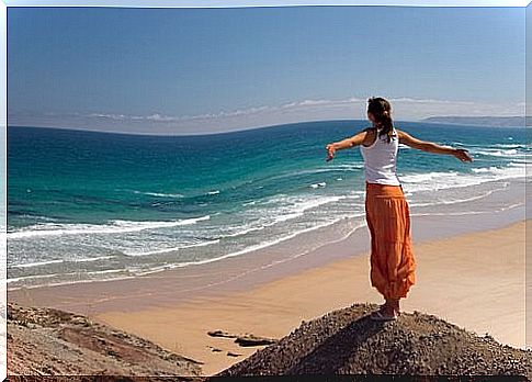 Woman standing with arms outstretched at a beach