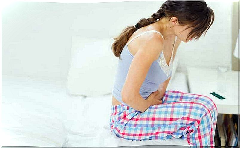 A woman sitting on the edge of a bed has abdominal pain