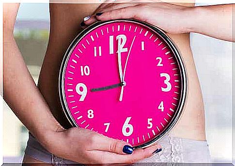 A woman holds a watch in front of her abdomen